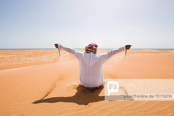 Beduine in Nationaltracht in der Wüste sitzend  Sand in der Hand  Wahiba Sands  Oman