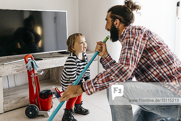 Vater und kleine Tochter amüsieren sich gemeinsam beim Putzen des Wohnzimmers