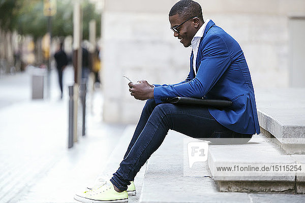 Young businessman wearing blue suit jacket,  sitting on step and using smartphone
