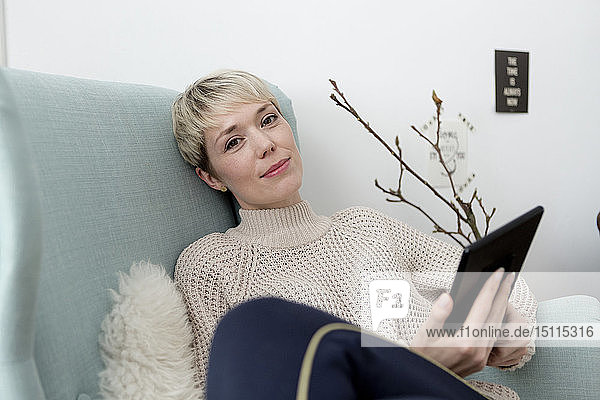 Porträt einer zu Hause im Sessel sitzenden Frau mit Tablette