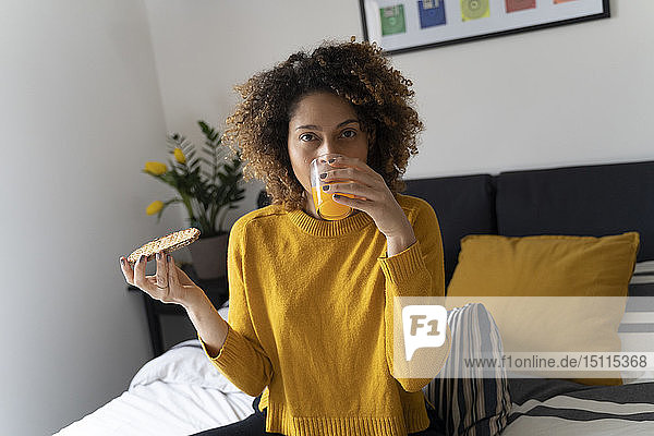 Frau sitzt auf dem Bett  trinkt Orangensaft  hält Toastbrot
