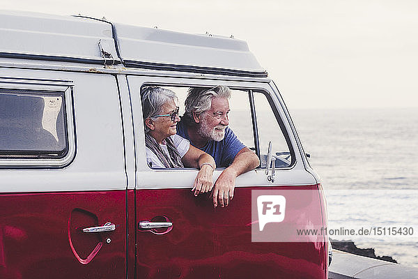 Älteres Ehepaar reist in einem Oldtimer-Van und schaut auf das Meer