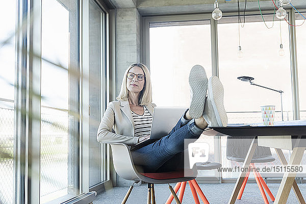 Relaxed businesswoman using laptop in office with feet up