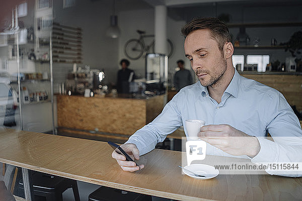 Successful businessman sitting in coffee shop  drinking coffee  using smartphone