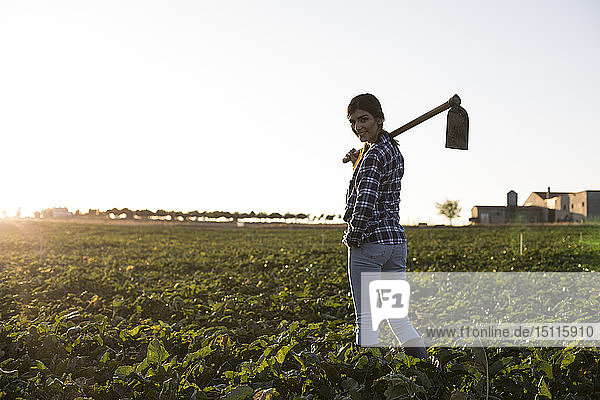 Young woman farmer with hoe on field  rear view