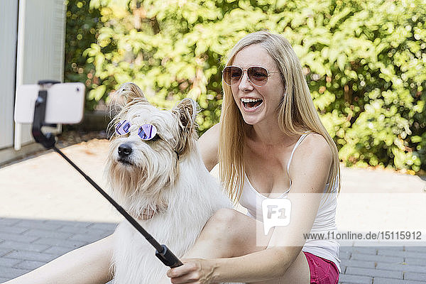 Happy woman taking a selfie with her dog wearing sunglasses