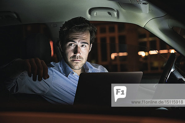 Young man with laptop in car at night
