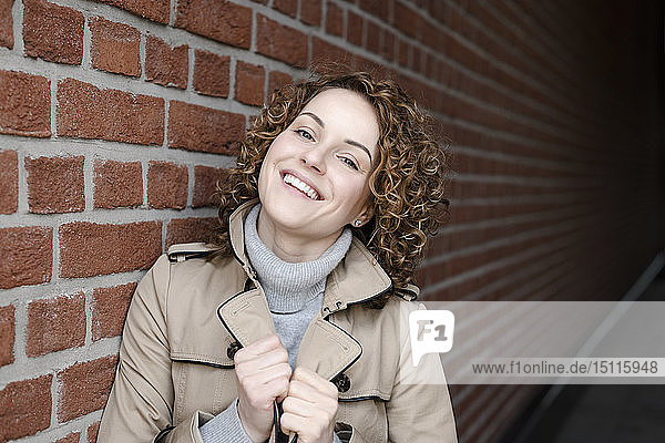 Bildnis einer lächelnden Frau mit lockigem Haar in Trenchcoat und Rollkragenpullover
