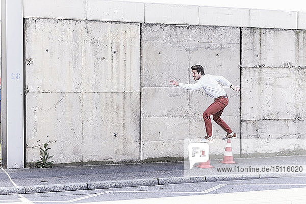 Junger Mann balanciert auf Verkehrskegeln vor einer Betonmauer