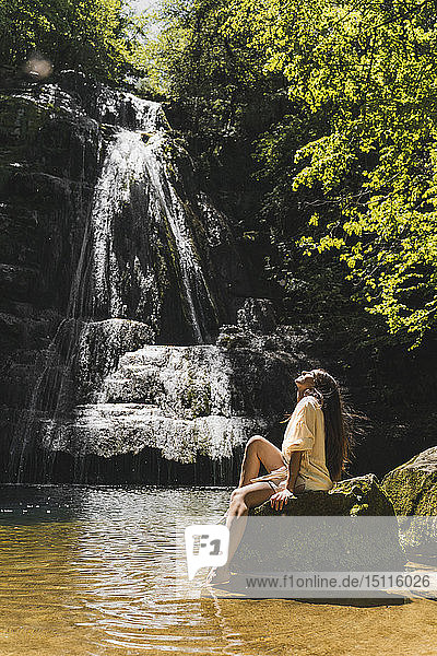 Young woman sitting on rock at a waterfall Garrotxa Spain