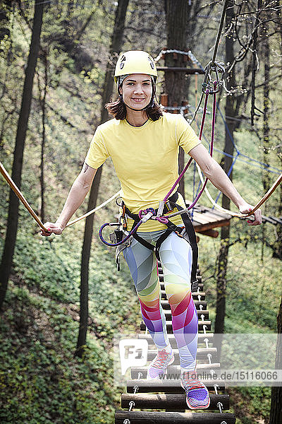 Junge Frau mit gelbem T-Shirt  Helm und Regenbogenhose in einem Seilgarten