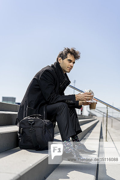 Businessman sitting on stairs having lunch break