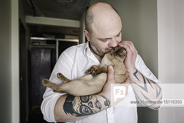 Tätowierter Mann kuschelt mit burmesischer Katze