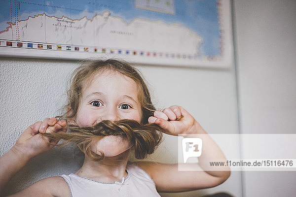 Porträt eines Mädchens  das mit ihren langen Haaren spielt und sich mit ihren Zöpfen einen Schnurrbart macht