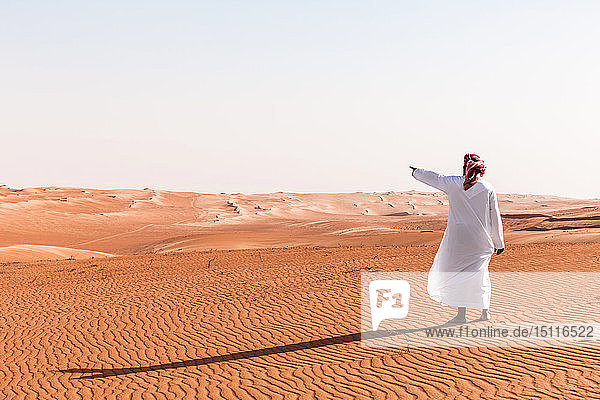 Beduine in Nationaltracht in der Wüste stehend  auf Distanz zeigend  Wahiba Sands  Oman
