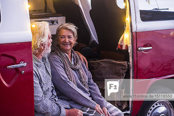 Älteres Ehepaar reist in einem Oldtimer-Van und betrachtet den Sonnenuntergang am Meer