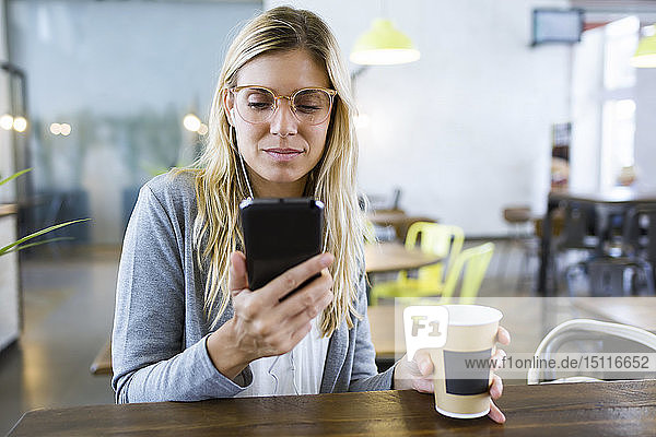 Junge Frau schreibt mit ihrem Handy SMS  während sie im Café Kaffee trinkt