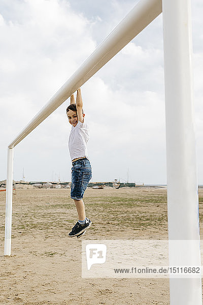 Boy hanging from the goal on the beach