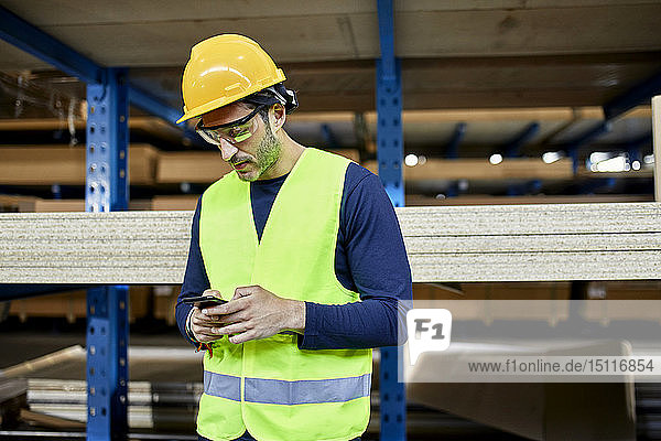 Arbeiter benutzt Mobiltelefon im Fabriklager