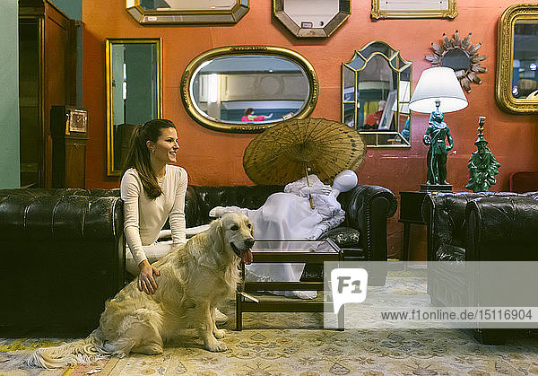 Lächelnde Frau mit Hund sitzt auf einer Couch in einem Vintage-Laden