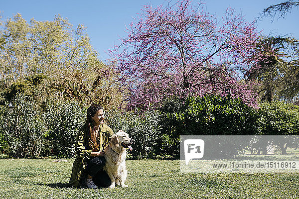 Glückliche Frau streichelt ihren Labrador Retriever auf einer Wiese im Stadtpark