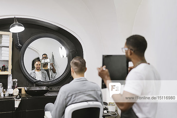 Friseur zeigt Mann im Friseursalon seinen Haarschnitt im Spiegel