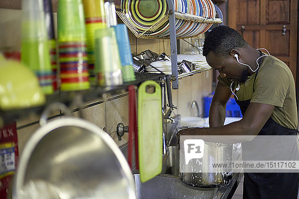 Young man washing dishes in restaurant kitchen  South Africa