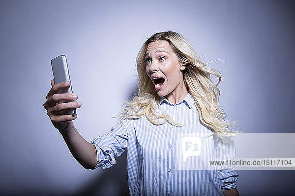 Porträt einer blonden Frau  die ein ausflippendes Smartphone betrachtet