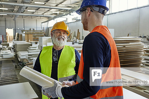 Two men with plan talking in factory