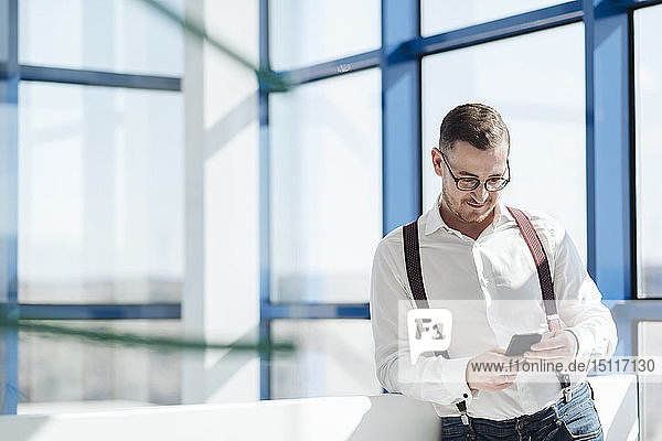 Geschäftsmann mit Handy am Fenster im modernen Büro