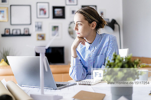 Frau im Büro schaut seitwärts mit dem Modell einer Windkraftanlage auf dem Tisch