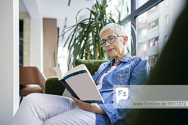 Ältere Frau sitzt auf dem Sofa und liest ein Buch