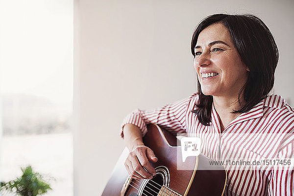Porträt einer lächelnden reifen Frau  die zu Hause Gitarre spielt