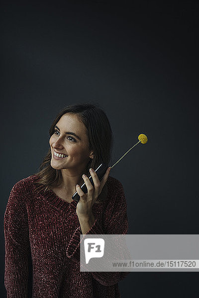 Smiling young woman using flower as antenna for cell phone
