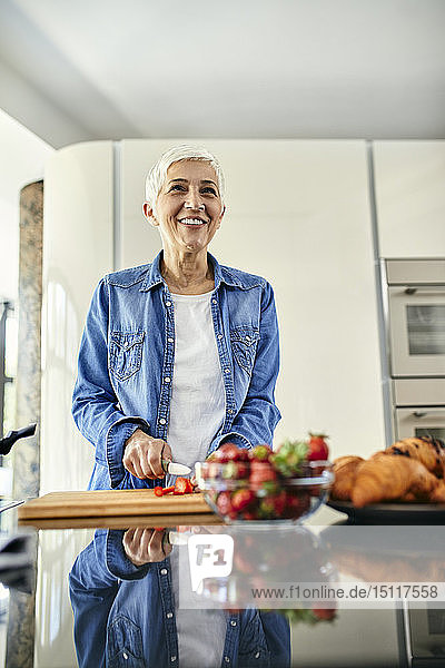 Ältere Frau steht in der Küche und schneidet Erdbeeren