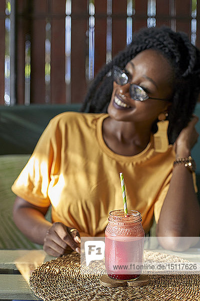 Lächelnde junge Frau mit Dreadlocks bei einem Smoothie in einem Café