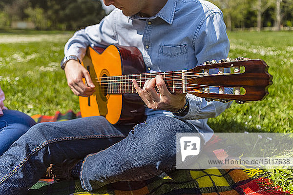 Junger Mann spielt Gitarre in einem Park