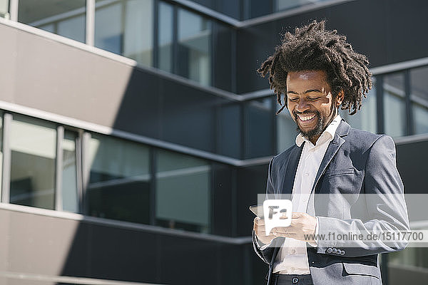 Lächelnder Geschäftsmann benutzt Mobiltelefon vor dem Büro