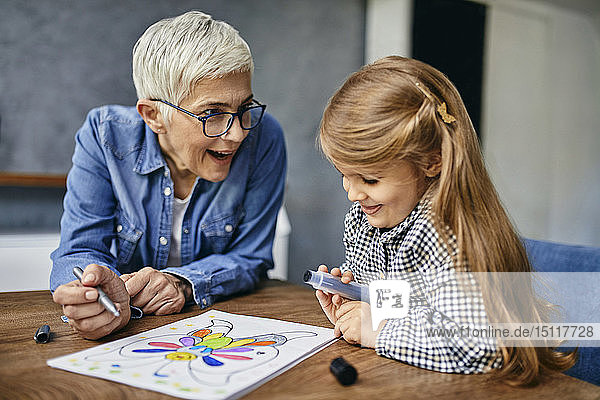 Großmutter und Enkelin sitzen am Tisch und malen ein Malbuch