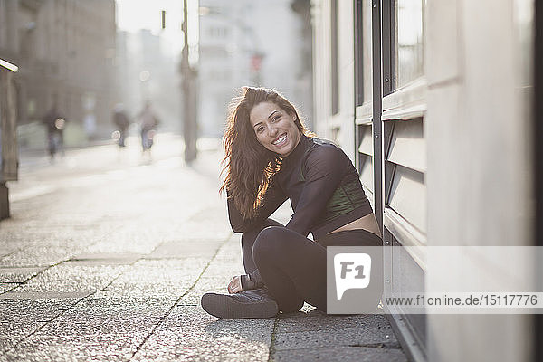 Porträt einer glücklichen  sportlichen jungen Frau  die in der Stadt auf dem Boden sitzt