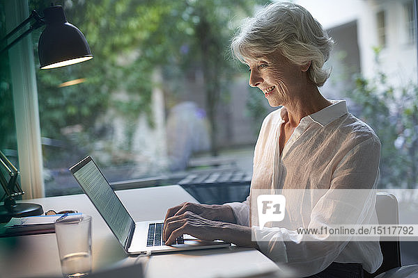 Smiling mature businesswoman sitting at desk using laptop