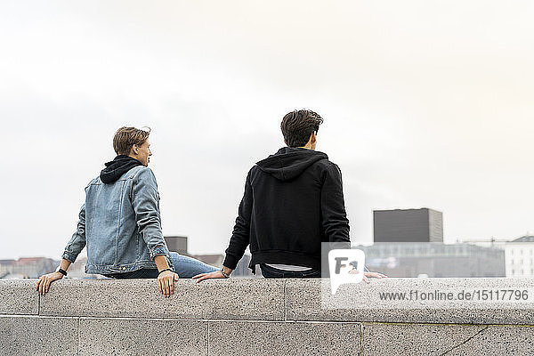 Dänemark  Kopenhagen  Rückansicht von zwei jungen Männern  die an einer Wand sitzen