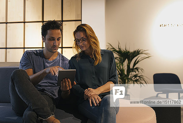 Young man and woman sitting on couch sharing tablet