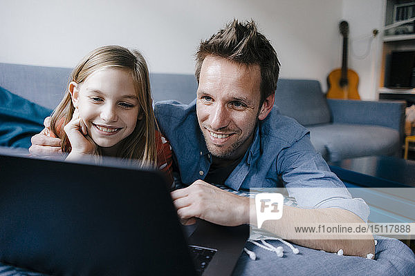 Glückliche Vater und Tochter liegen zu Hause auf der Couch und benutzen einen Laptop