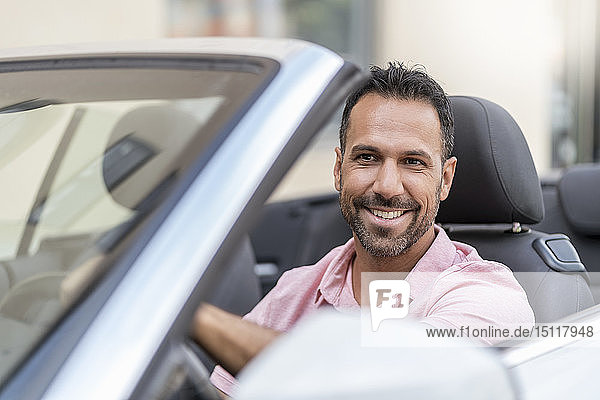 Porträt eines lächelnden Mannes am Steuer eines Cabrios