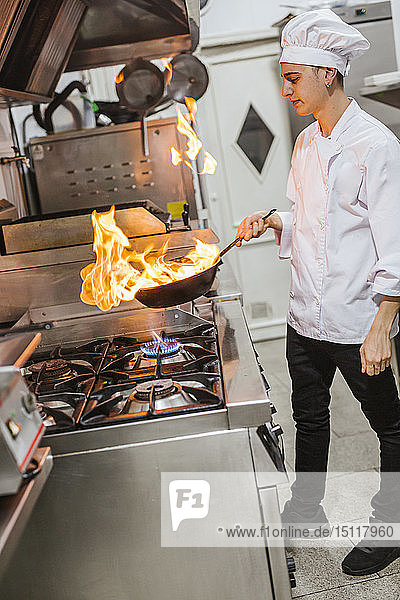 Junior chef with pan of flames in traditional spanish restaurant kitchen