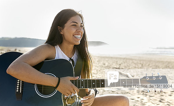 Glückliche junge Frau mit Gitarre am Strand