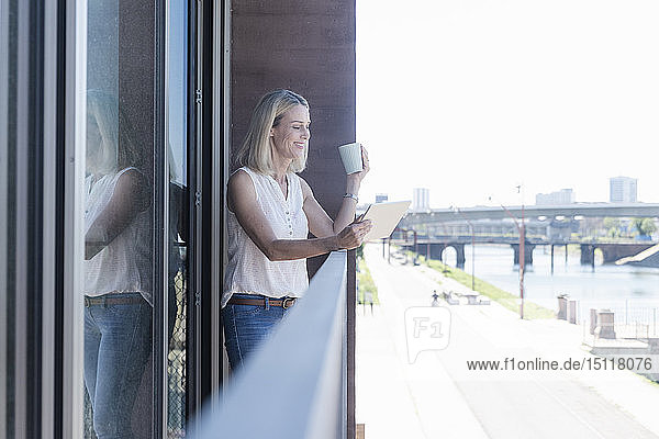 Lässige Geschäftsfrau steht mit Tablette auf dem Balkon