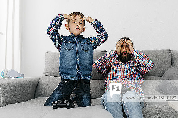 Porträt von Vater und Sohn zusammen auf der Couch beim Computerspiel