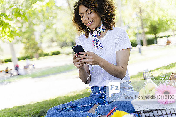 Entspannte Frau mit Handy und Kopfhörern beim Picknick im Park